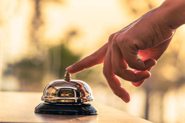 istockphoto-1330958468-612×612 Woman cook, waitress of beach restaurant ringing service bell to warn that the dish is ready. Roof of cafe sea and palm tree view on sunset.